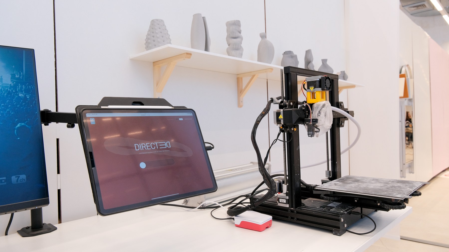 DIRECTED's exhibit setup: a tablet interface connected to a clay printer, with printed forms behind it