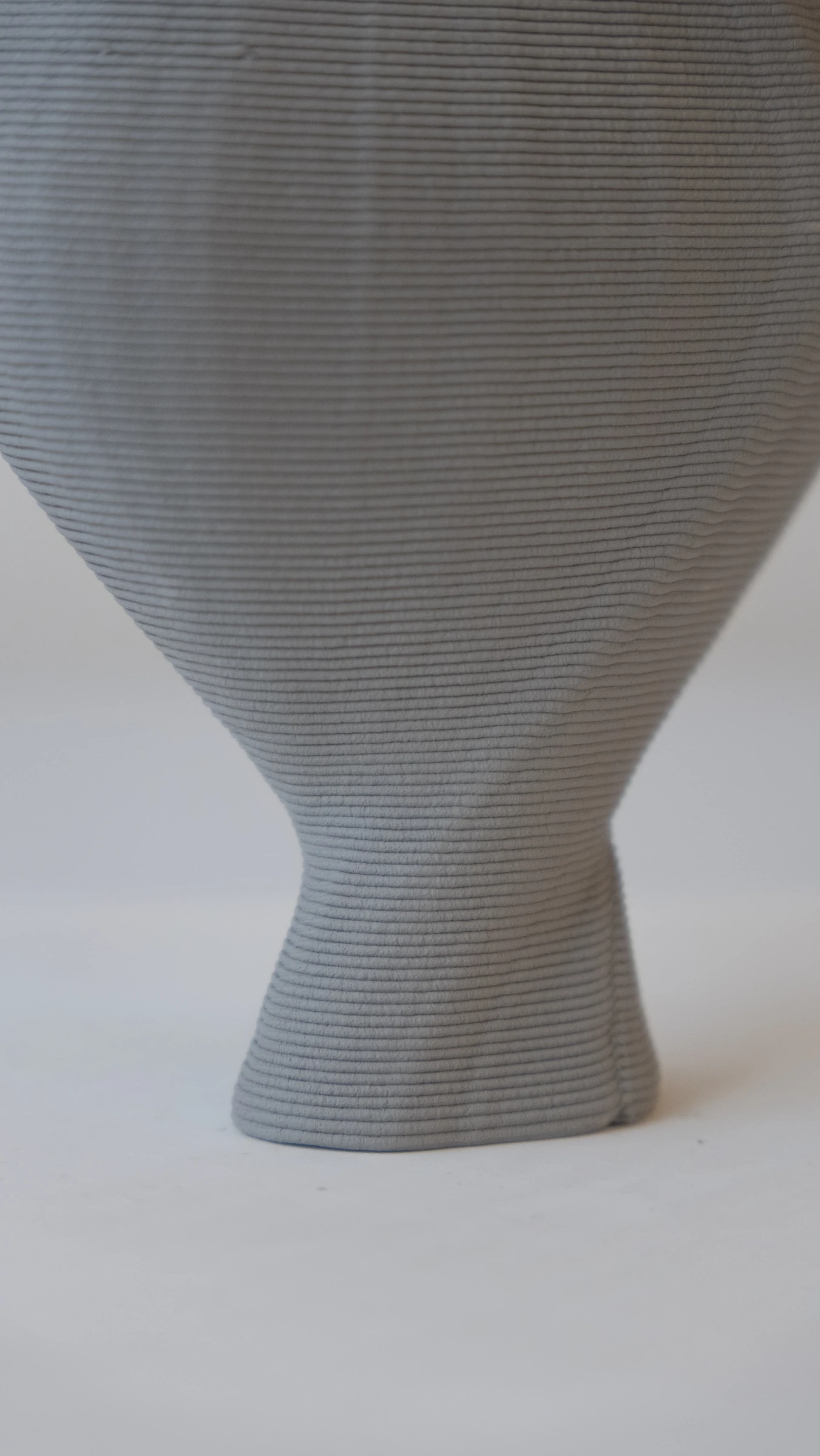 Close-up of a printed clay form widening above a narrow base, with individual deposited layers visible
